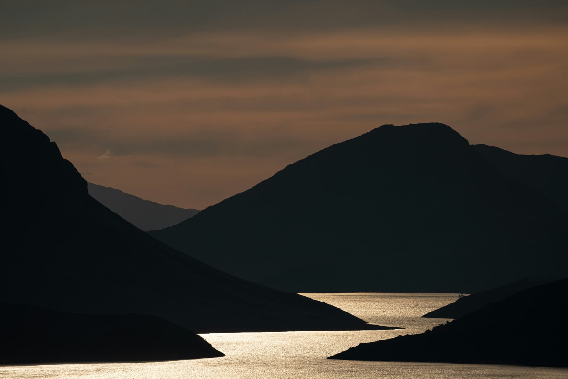 Layered mountain ridge silhouettes framing a channel of backlit water at sunset in southern Tasmania